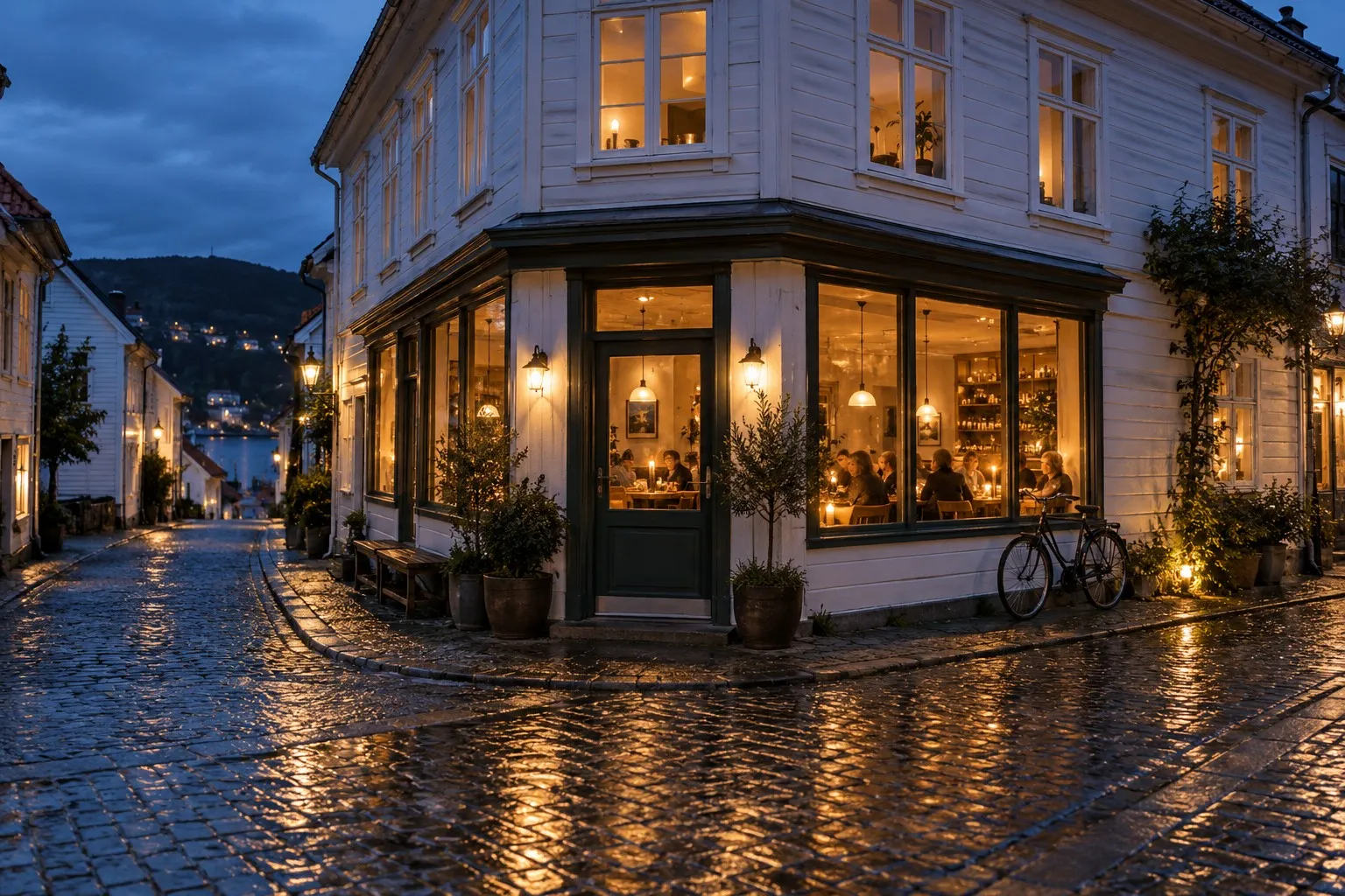 Restaurant i et gammelt hvitt trehus i blåtimen, med varmt lys i vinduene